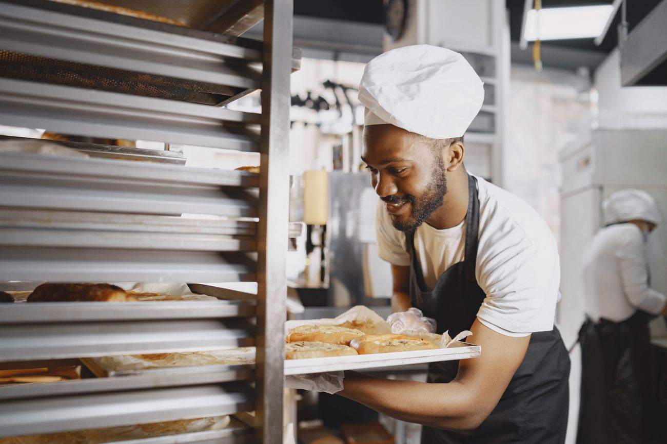 A baker pulling trays from a rack in a commercial kitchen